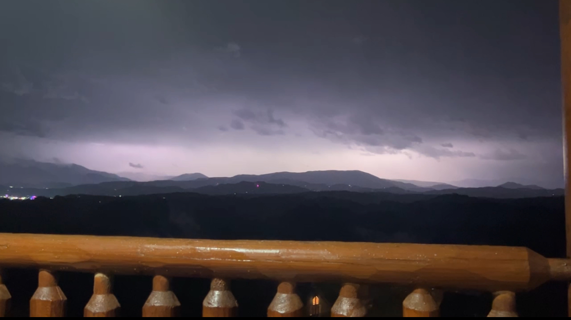 A dark, black valley contrasted by a white sky from a lightning strike. The strike highlights a mountain range in front of it.